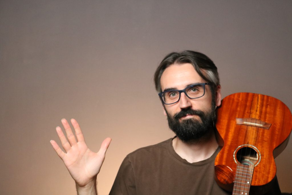 Hombre con guitarra saludando alegremente.